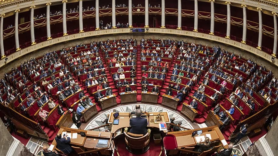 L'hémicycle de l'Assemblée nationale en séance, vu d'en haut : les députés dans les travées rouges en demi-cercle, le perchoir et la tribune au centre.