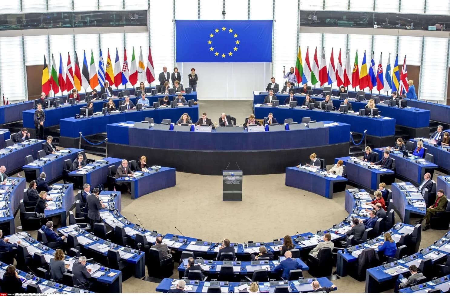 L'hémicycle du Parlement européen à Strasbourg en séance plénière : les députés en demi-cercle, la tribune au centre, les drapeaux des États membres et le drapeau européen au fond.
