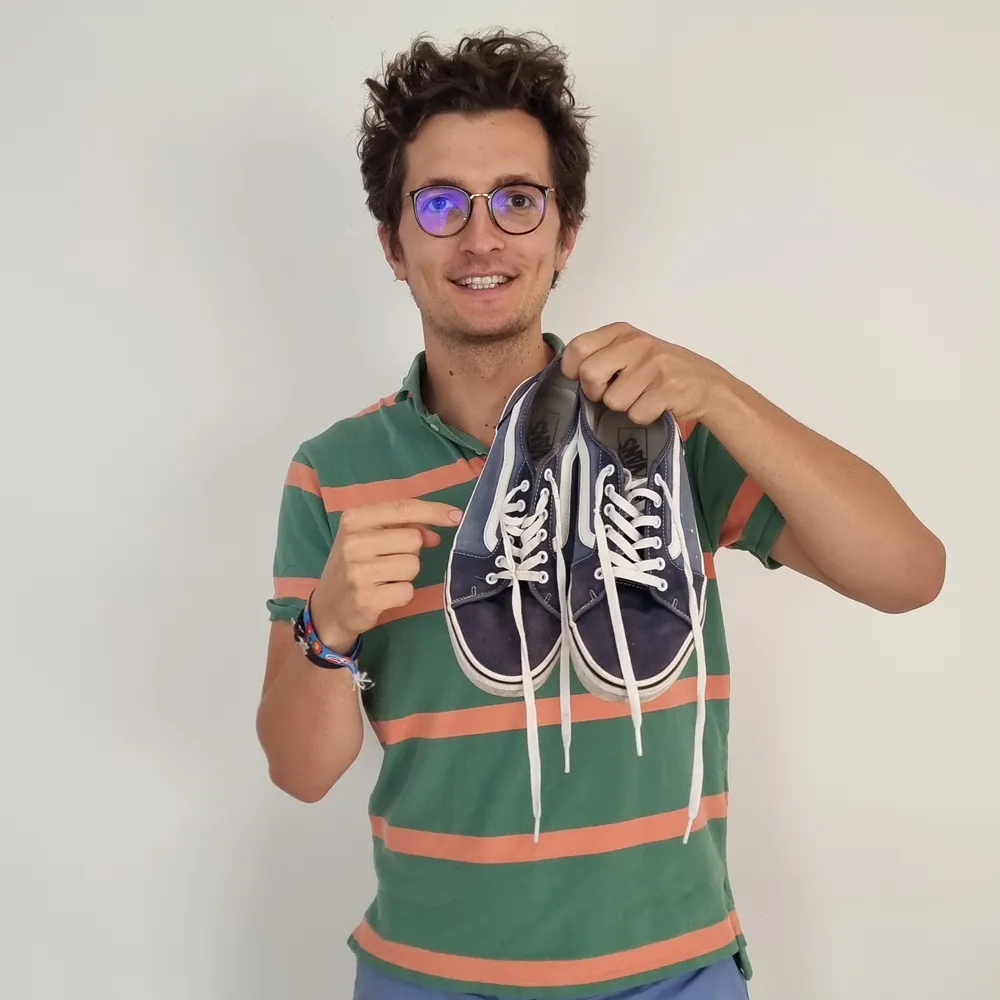 Stanislas tient une paire de baskets en toile bleu marine achetée d'occasion sur Vinted et la montre du doigt