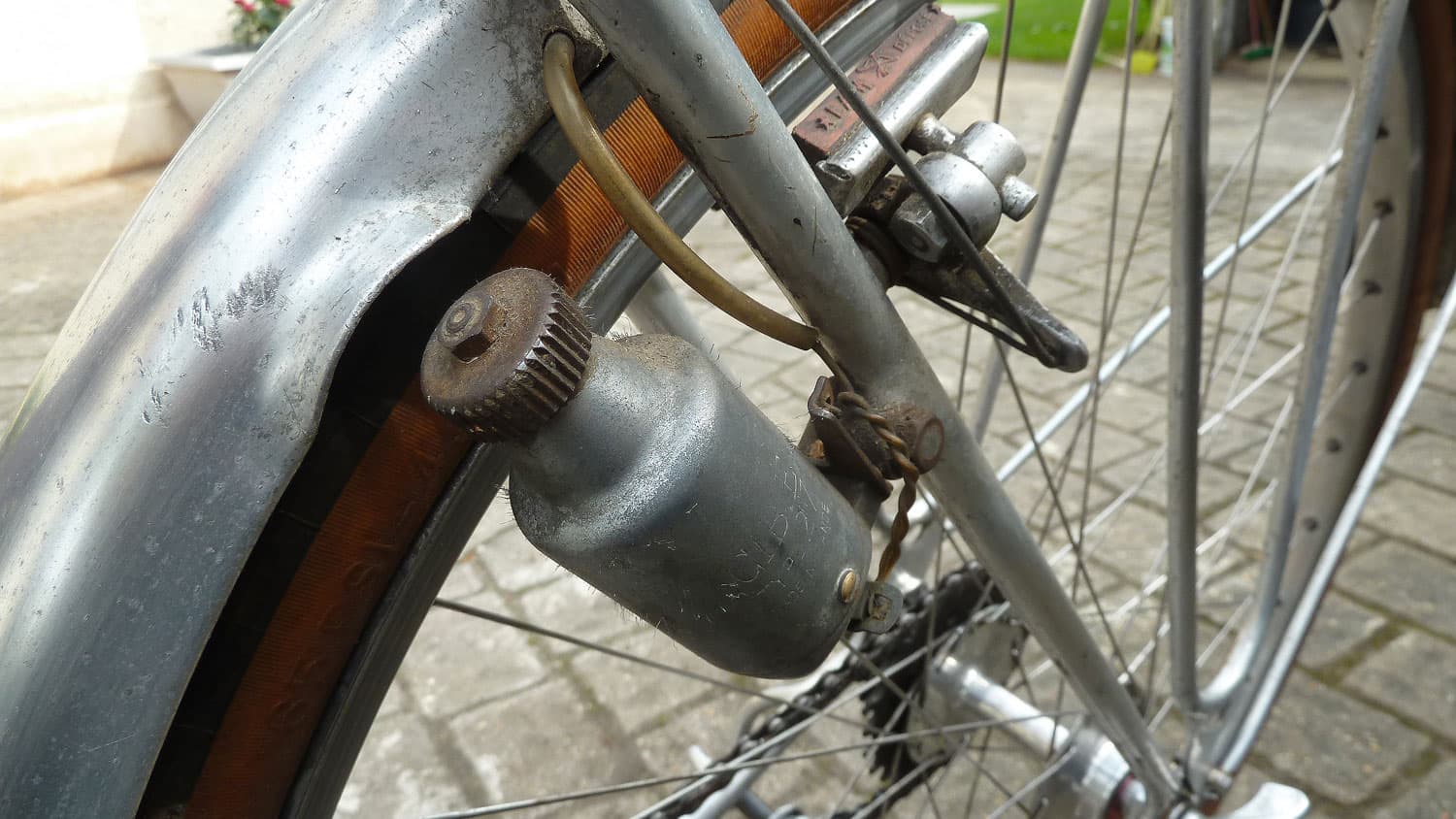 Dynamo bouteille fixée sur la fourche d'un vélo ancien, sa molette crantée tournée vers le flanc du pneu